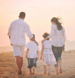 young mother and father walking on beach with their two young children